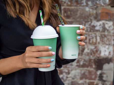 disposable paper straws in compostable cold drink cups with domed lids being held by a customer leaving a cafe