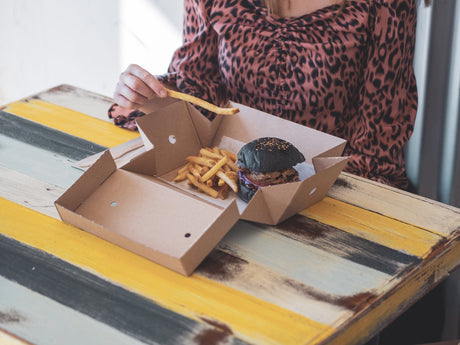 a woman eating a burger and chips from a compostable kraft takeaway meal box