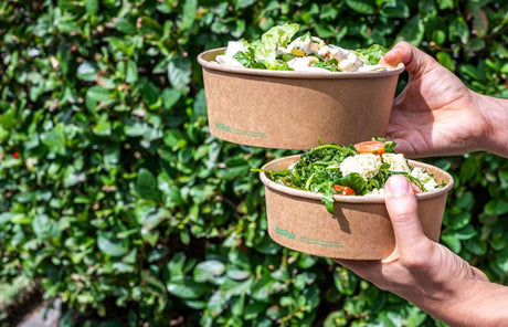 kraft paper salad bowls made from recycled kraft paper and lined with pla held out in front of a green tree