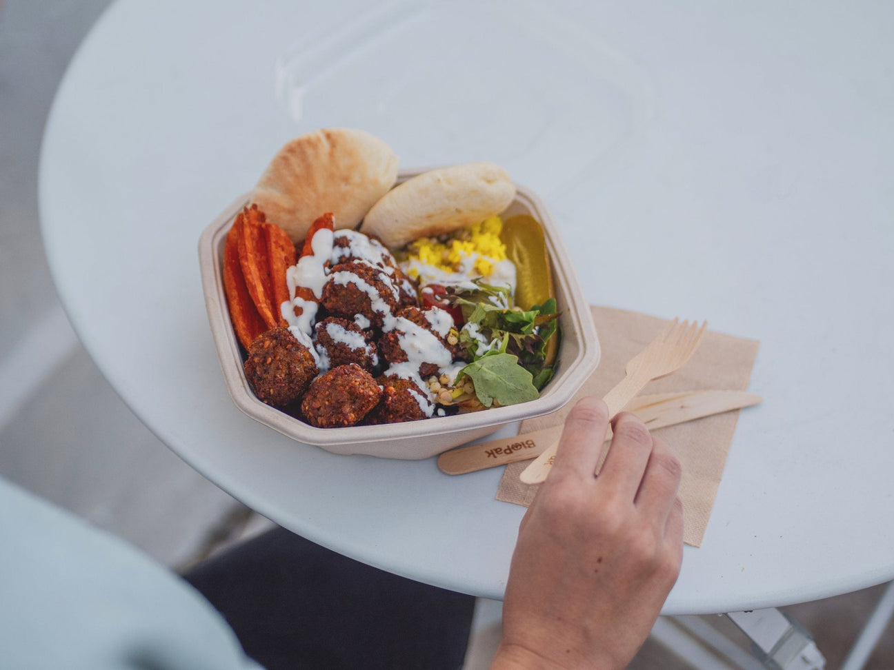 takeout falafel salad in a octagonal takeaway container with wooden cutlery and kraft napkin